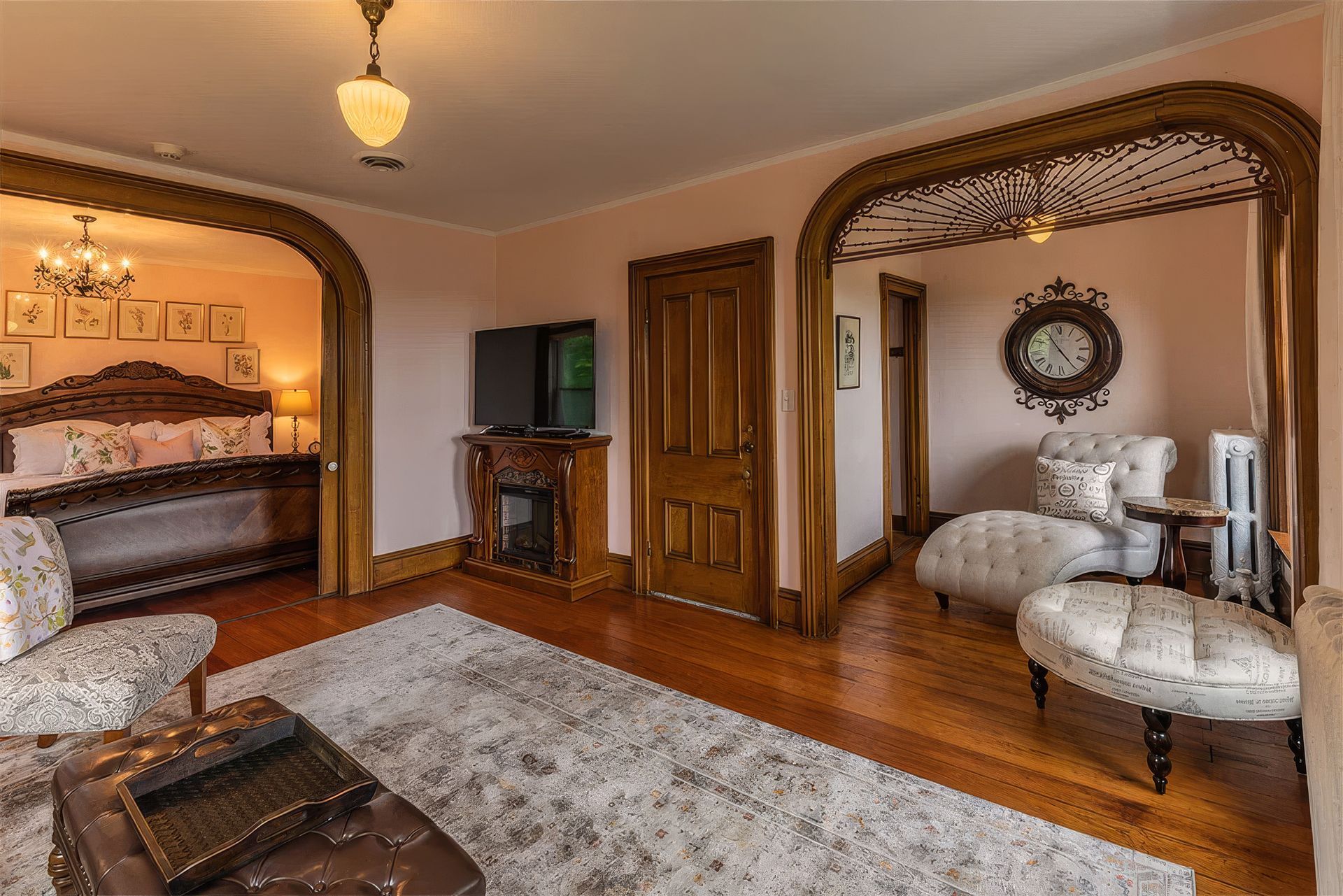 Elegant bedroom with carved wood arches, a four-poster bed, fireplace, and white upholstered chairs