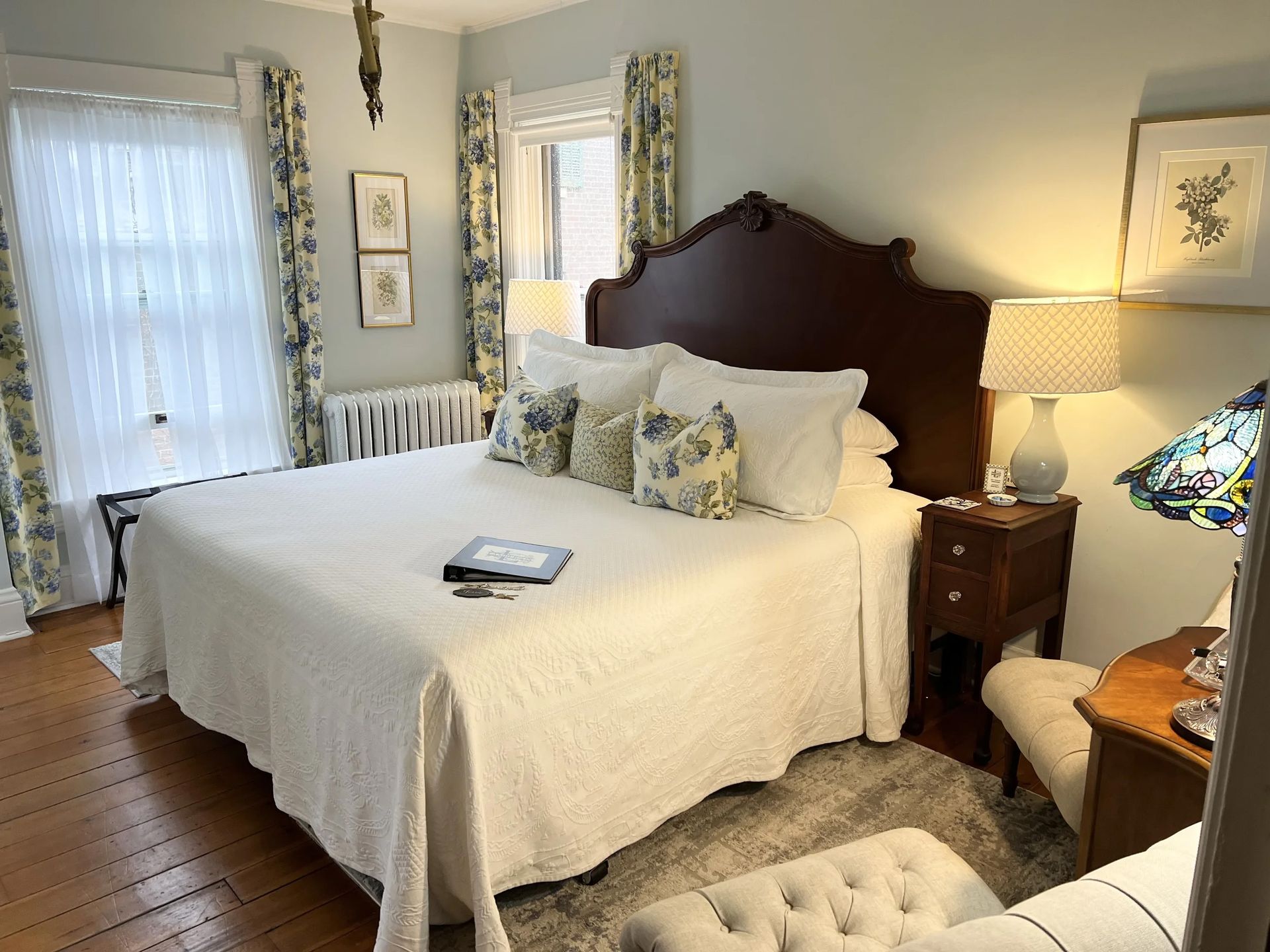 Bright bedroom with a white bed, dark wood headboard, nightstand lamps, and hardwood floors