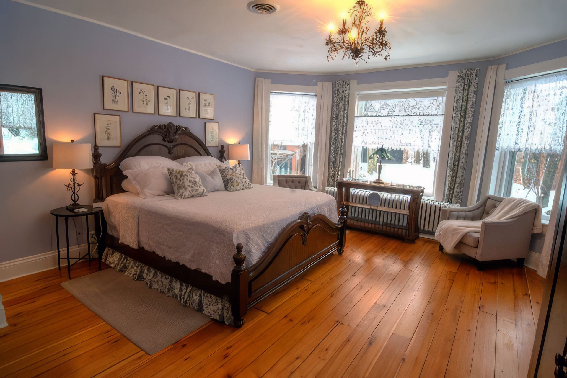 Spacious bedroom with a bed, chandelier, hardwood floors, and bay windows with seating.