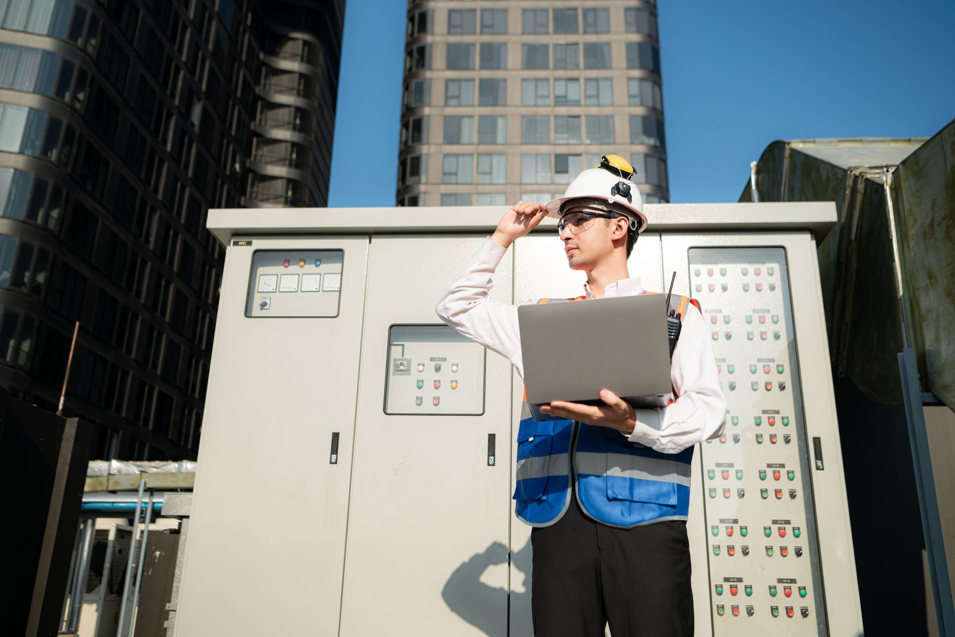 A man is standing in front of a building holding a laptop.