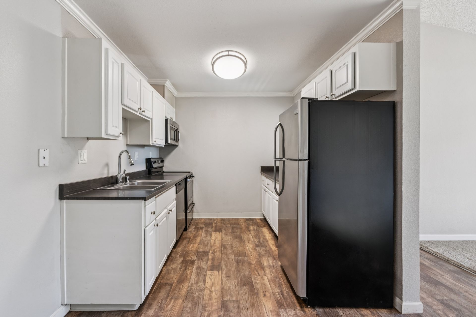 Narrow white kitchen with stainless steel appliances, dark countertops, and wood-look flooring