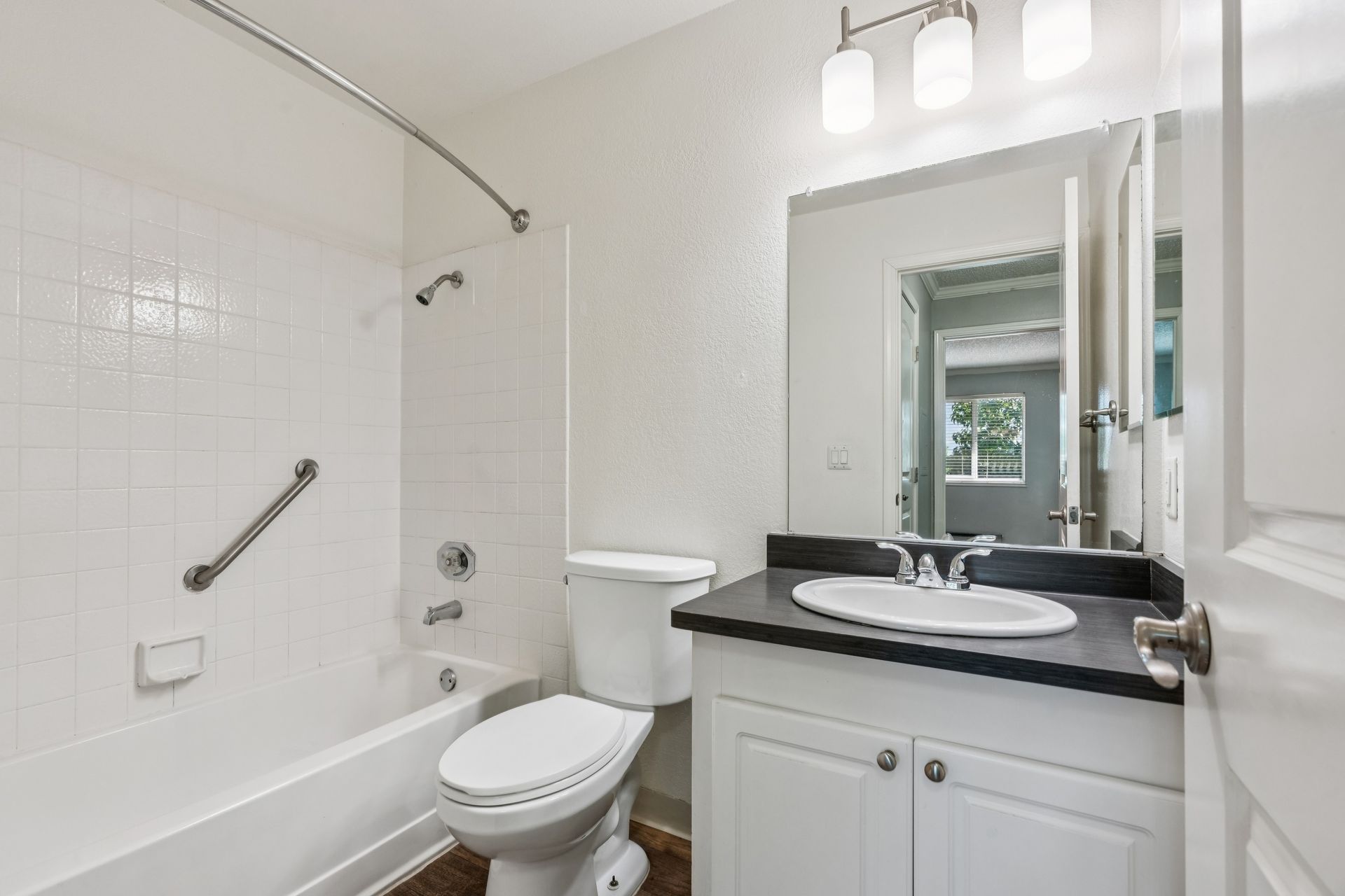Bright white bathroom with tub, toilet, vanity, and large mirror under vanity lights.