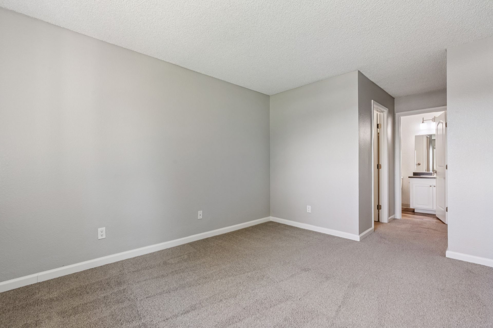 Empty beige carpeted room with light gray walls and a doorway to a bathroom