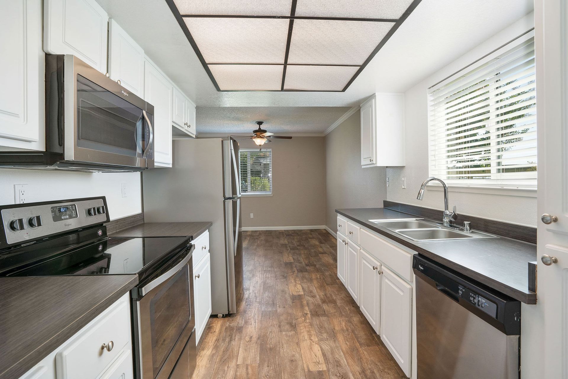 Kitchen with white cabinets, stainless steel appliances, and wood-look flooring at Ridgecrest Apartment Homes.