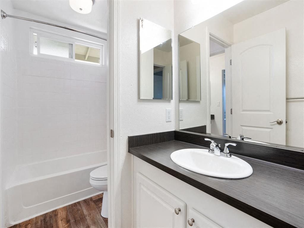 Bathroom with white sink, dark countertop, large mirror, and a bathtub/shower at Ridgecrest Apartment Homes.