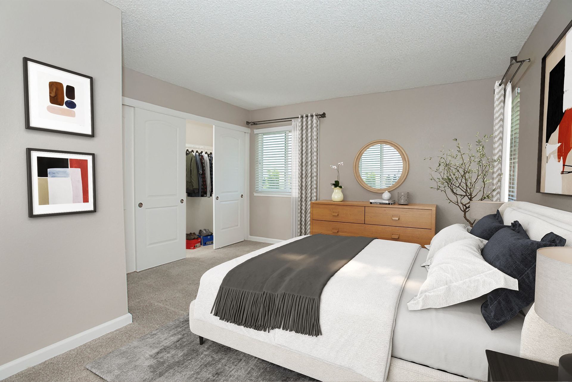 Bedroom in apartment with bed, dresser, circular mirror, and open closet at Ridgecrest Apartment Homes.