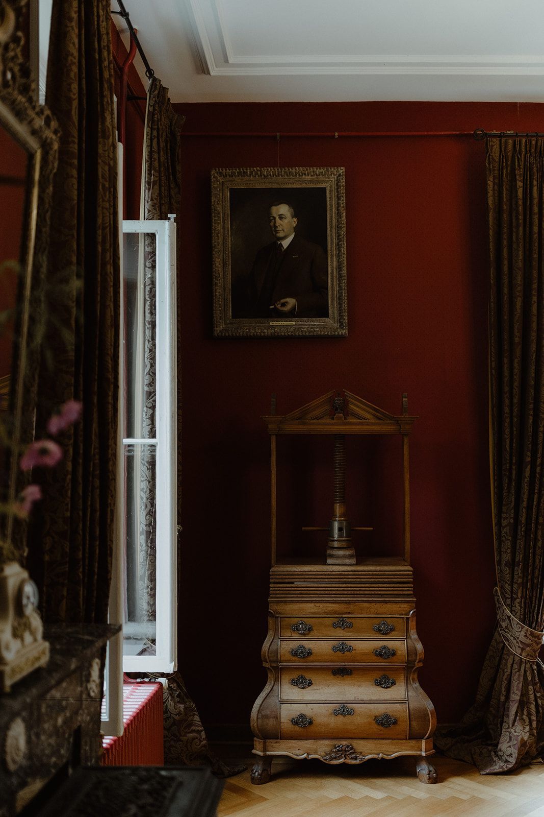 Een kamer met rode muren, een ladekast, een spiegel en een schilderij aan de muur.