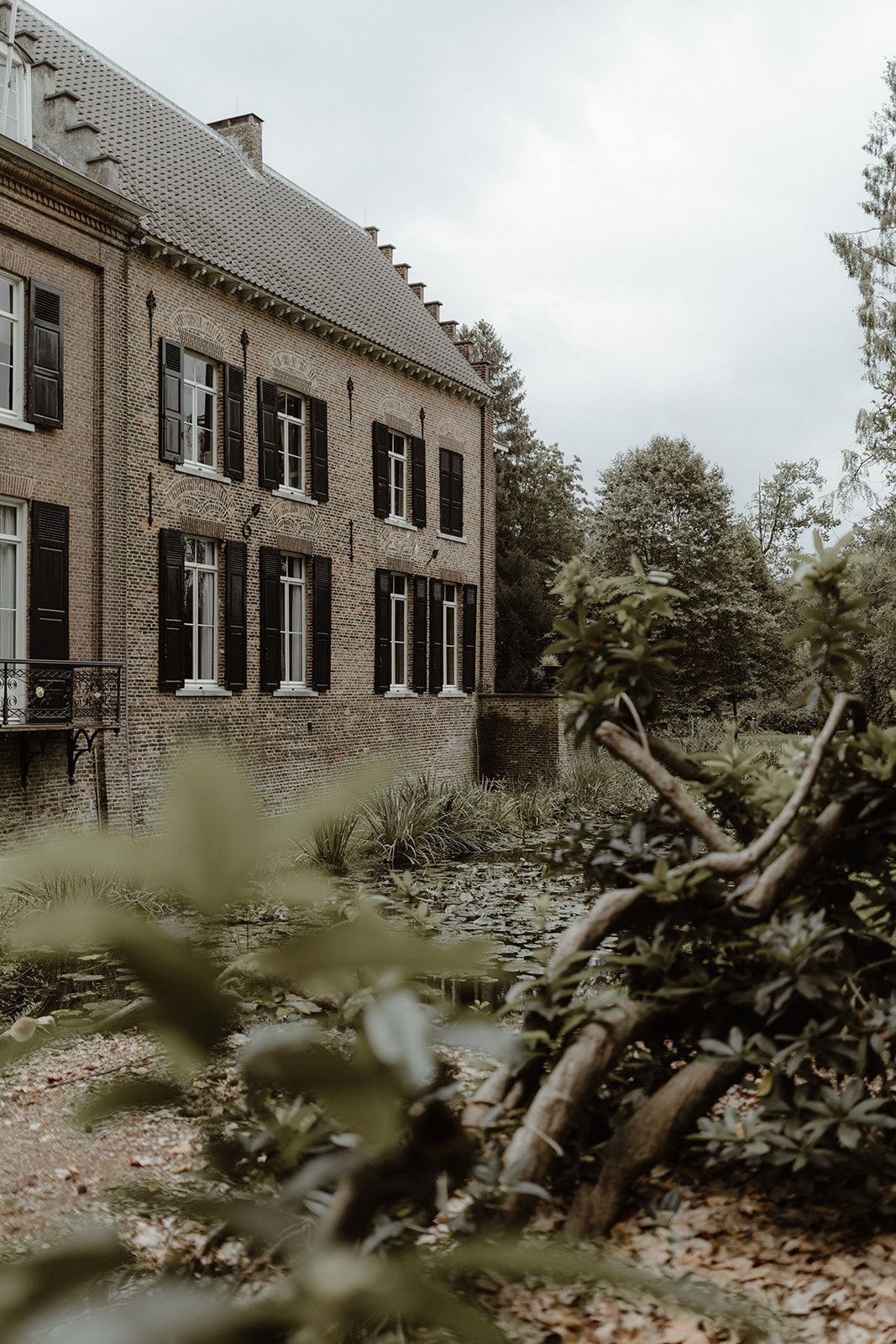 Een bakstenen gebouw met zwarte luiken en een boom ervoor.