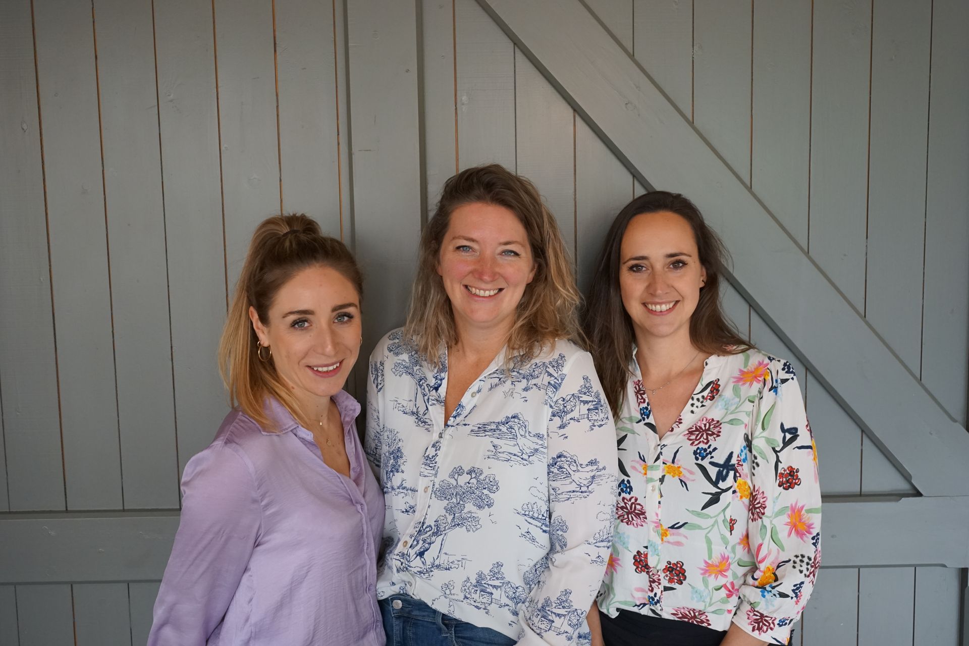 Drie vrouwen poseren voor een foto voor een houten wand.