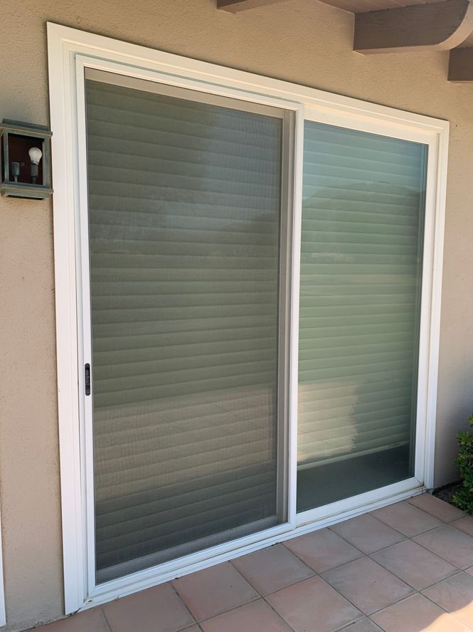 A white sliding glass door with blinds on a tiled patio.