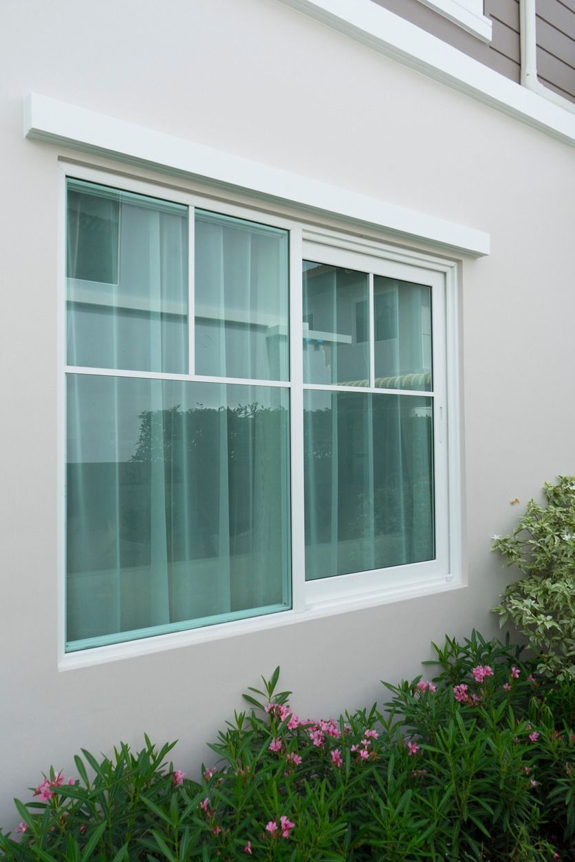 A large window on the side of a house with flowers in the background.