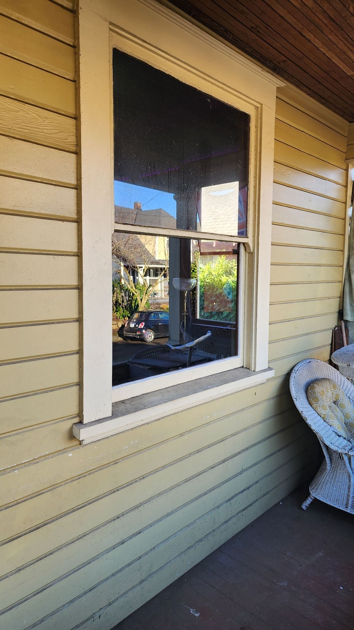 A window on the side of a house with a wicker chair on the porch.