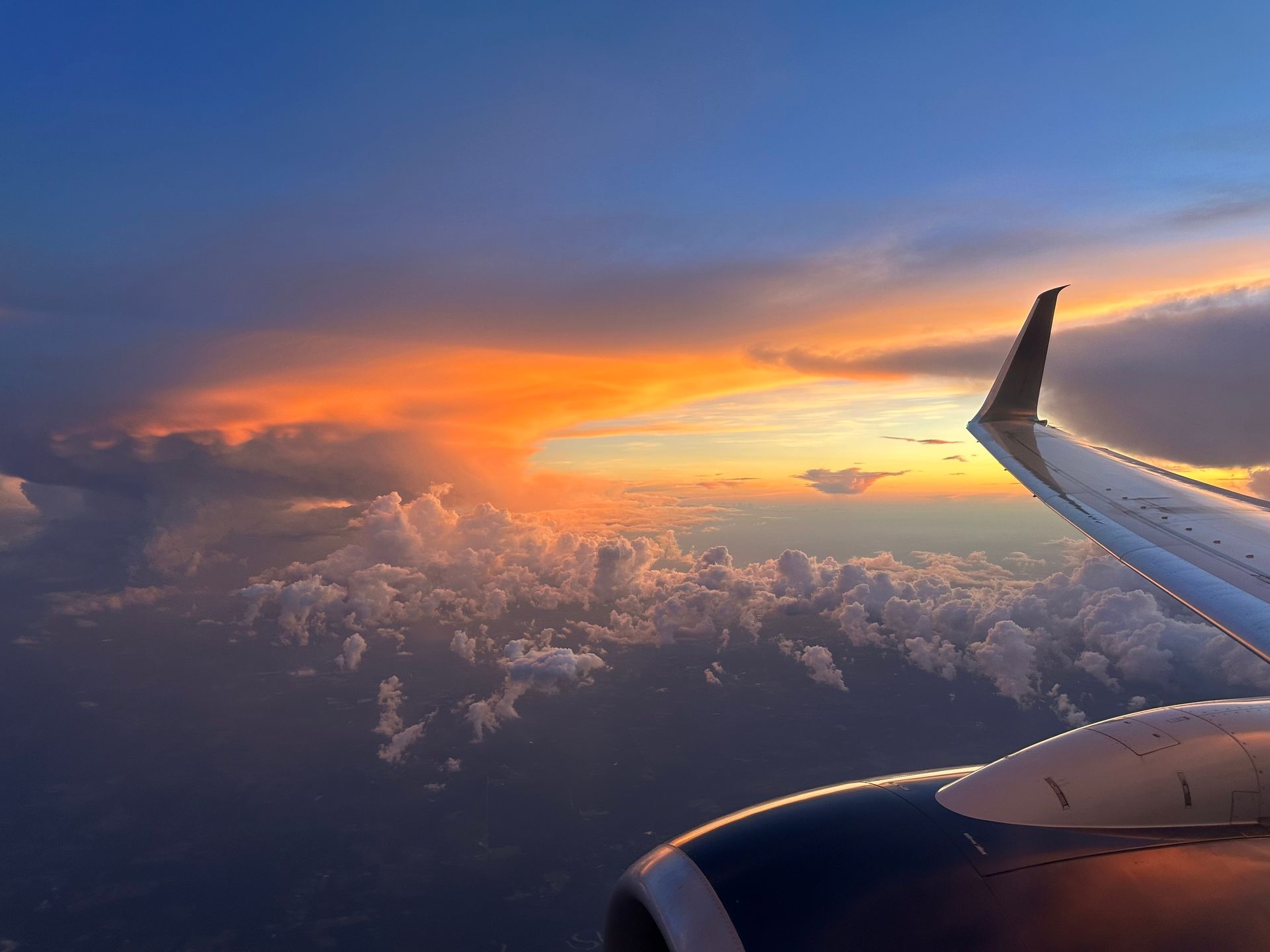 Airplane wing in flight, vibrant sunset colors illuminate clouds below.
