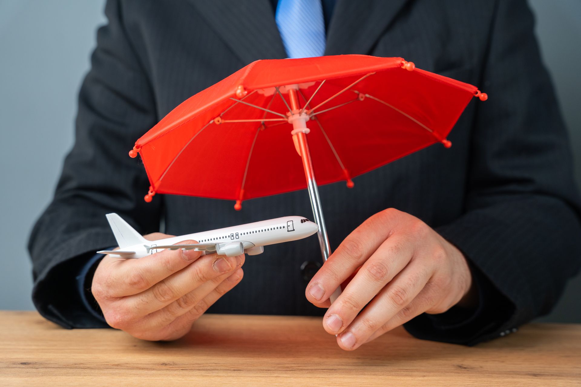 Man in suit holding a toy airplane under a small red umbrella.