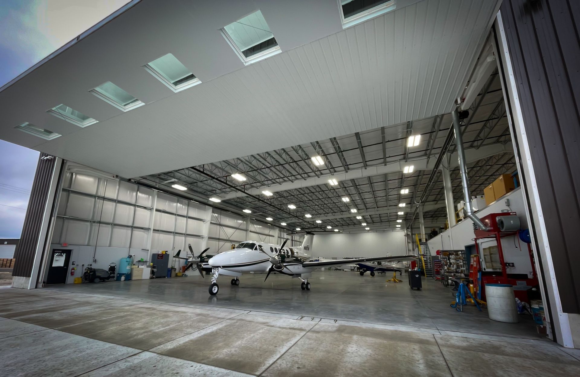 Small airplane in a hangar with open doors and bright overhead lights