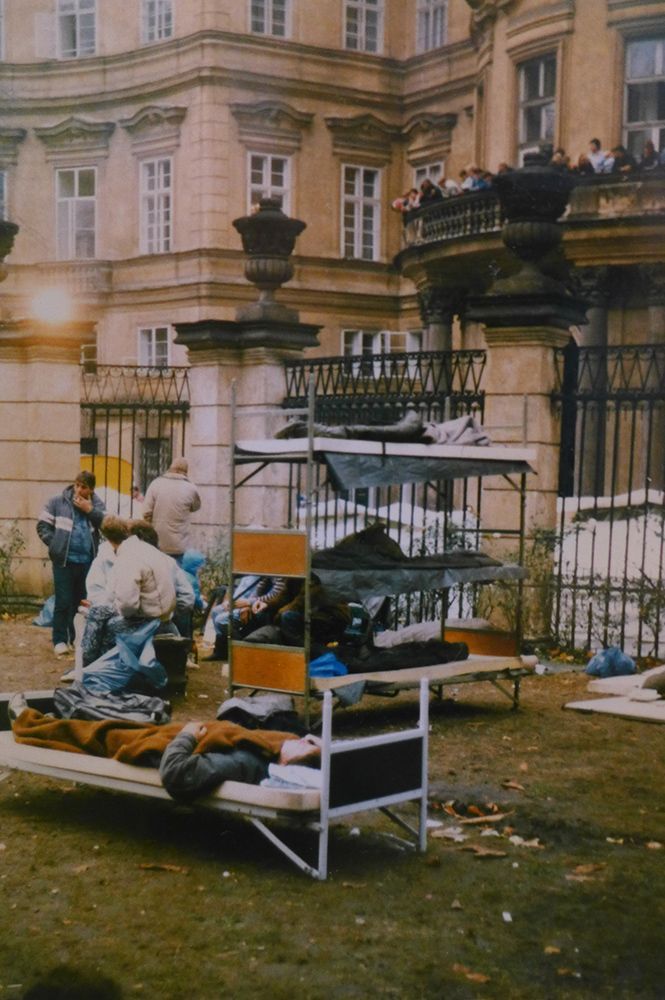Workers sort items on a cart outside a grand building with wrought-iron fencing.