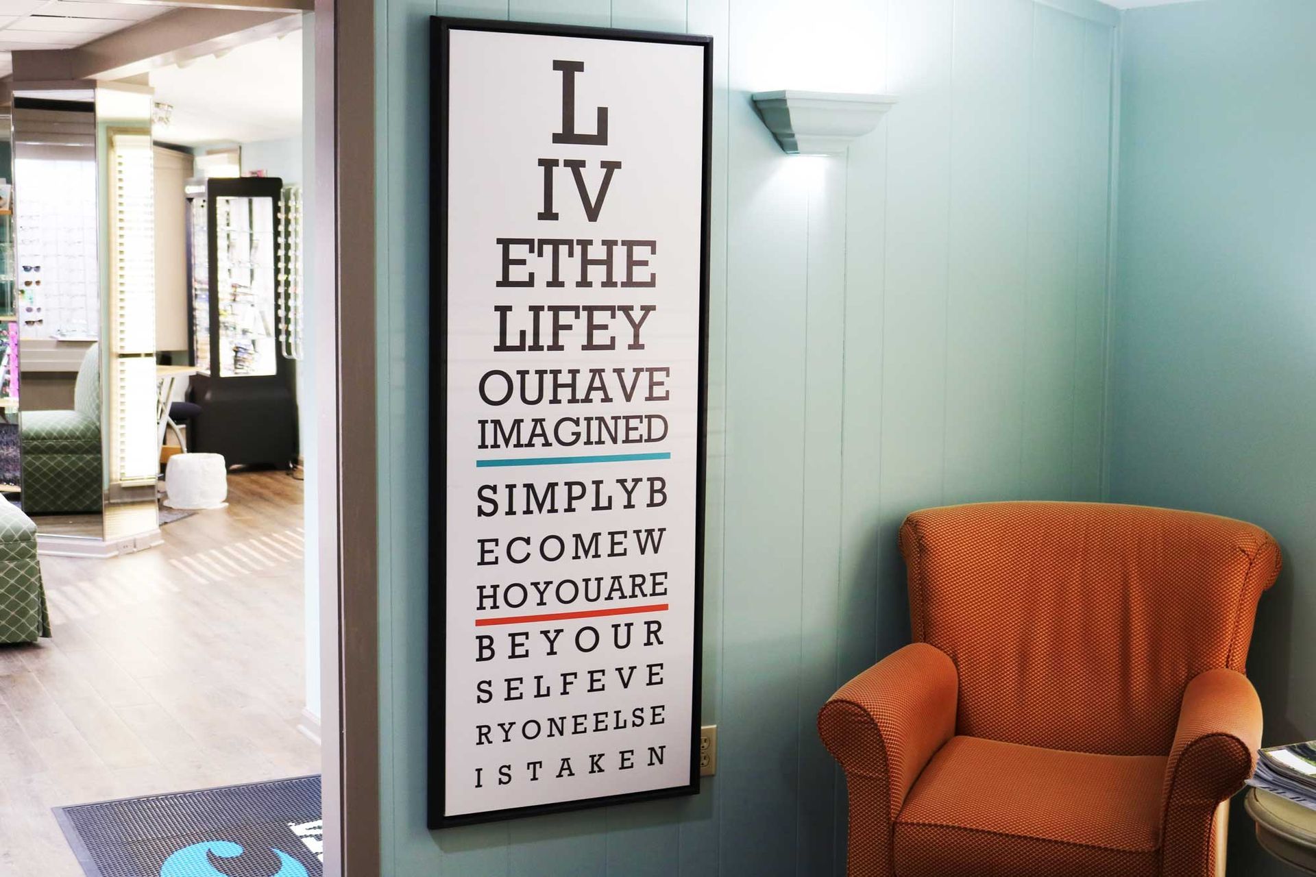 Eye chart art on a blue wall next to an orange armchair in a waiting room.