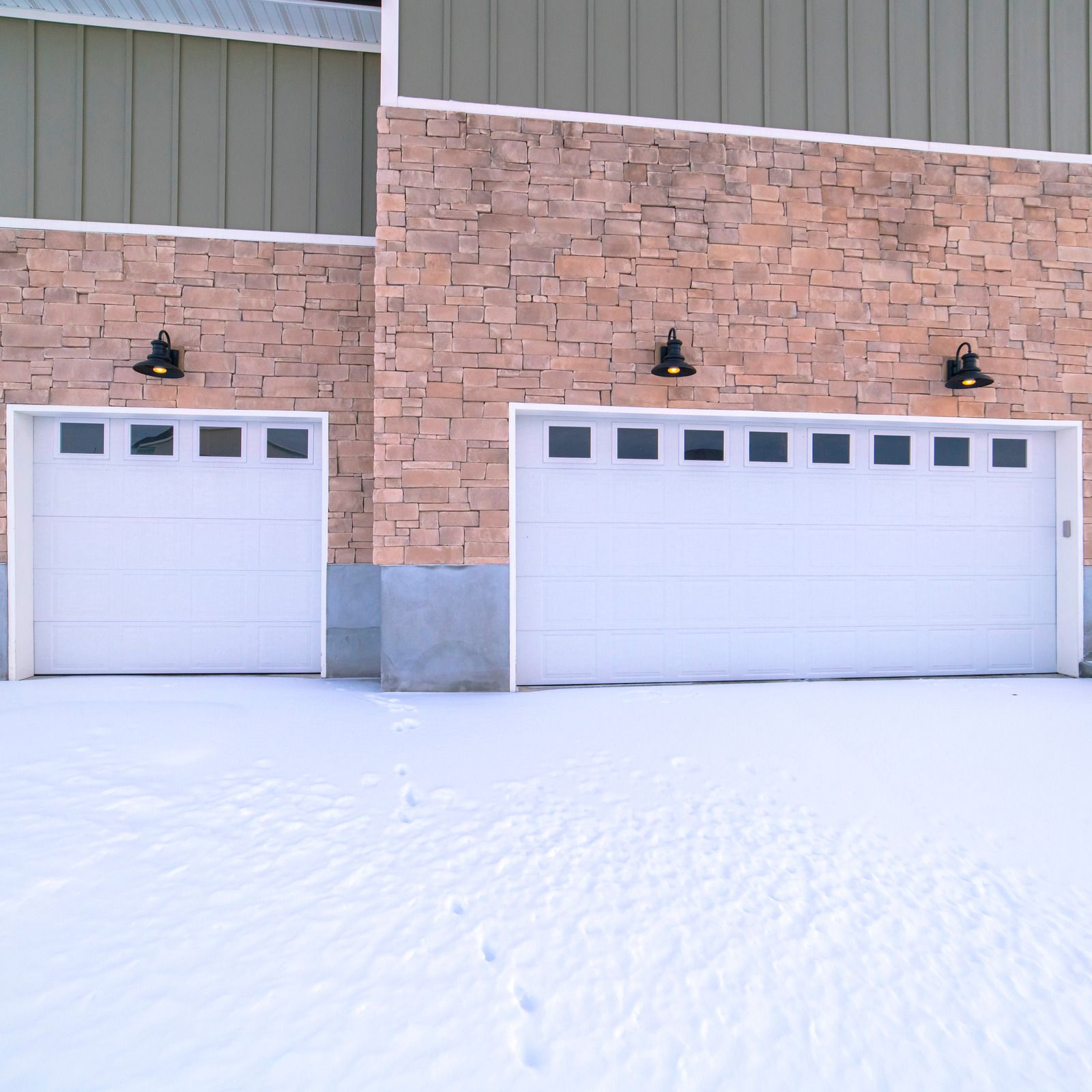 Snow-covered building exterior with two white garage doors and stone facade
