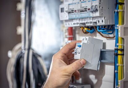 Colocación manual de un interruptor automático blanco en un panel eléctrico con cables e interruptores visibles.