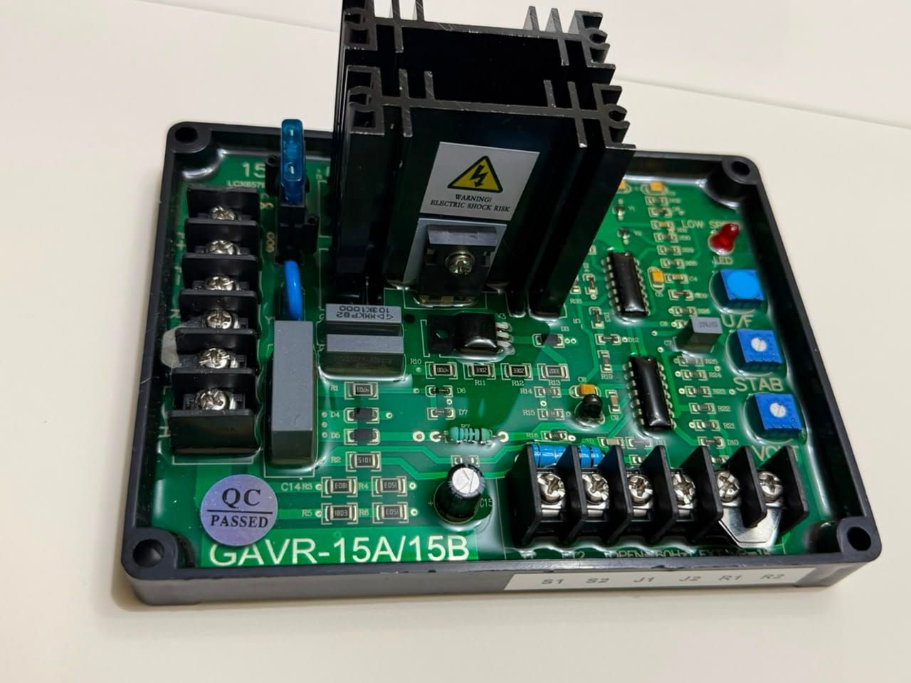 Placa de circuito de control electrónico abierta con disipador de calor negro, PCB verde y componentes azules/rojos.