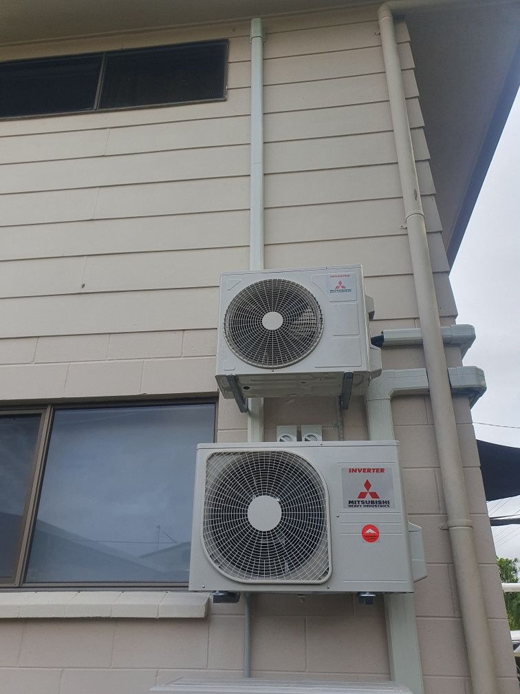 Two Mitsubishi air conditioning units mounted on a light-colored building exterior.— Cool Tropics Air Conditioning & Refrigeration in Mourilyan Harbour, QLD