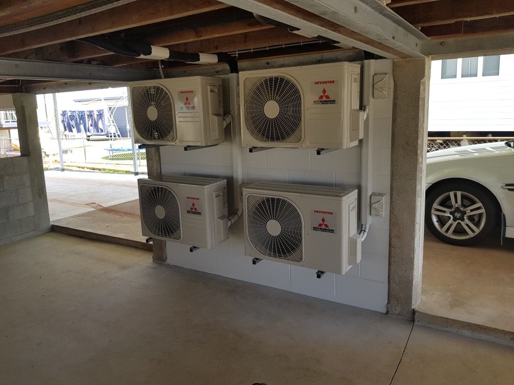 Four Mitsubishi air conditioning units mounted on a wall under a building with a car visible.— Cool Tropics Air Conditioning & Refrigeration in Tully, QLD