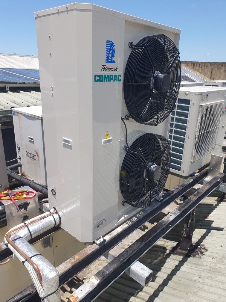 An outdoor HVAC unit with two black fans. On a roof, with solar panels visible in background.— Cool Tropics Air Conditioning & Refrigeration in Mourilyan Harbour, QLD