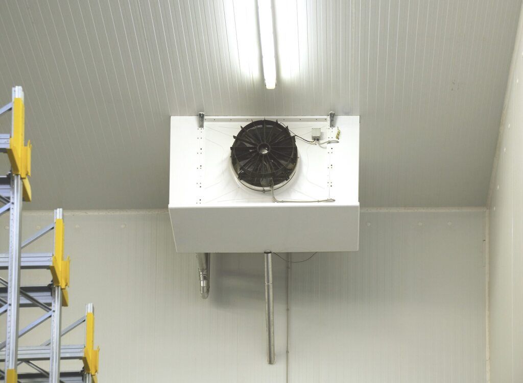 A cold storage unit with a ceiling-mounted evaporator fan, racks and bright lights.— Cool Tropics Air Conditioning & Refrigeration in Cardwell, QLD