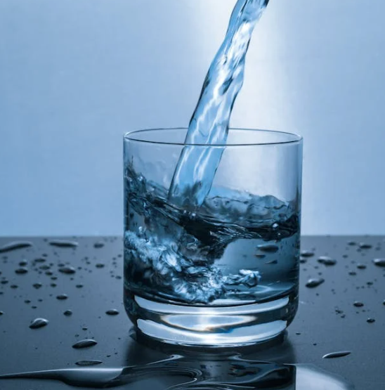 Water pouring into a clear glass on a dark surface, with splashes and droplets around it.