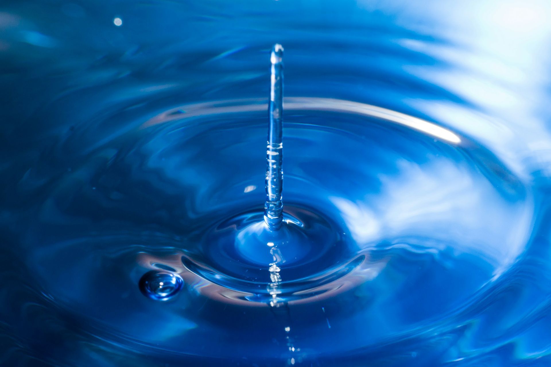 Water droplet splashing into a blue surface, creating concentric ripples and a rising splash column