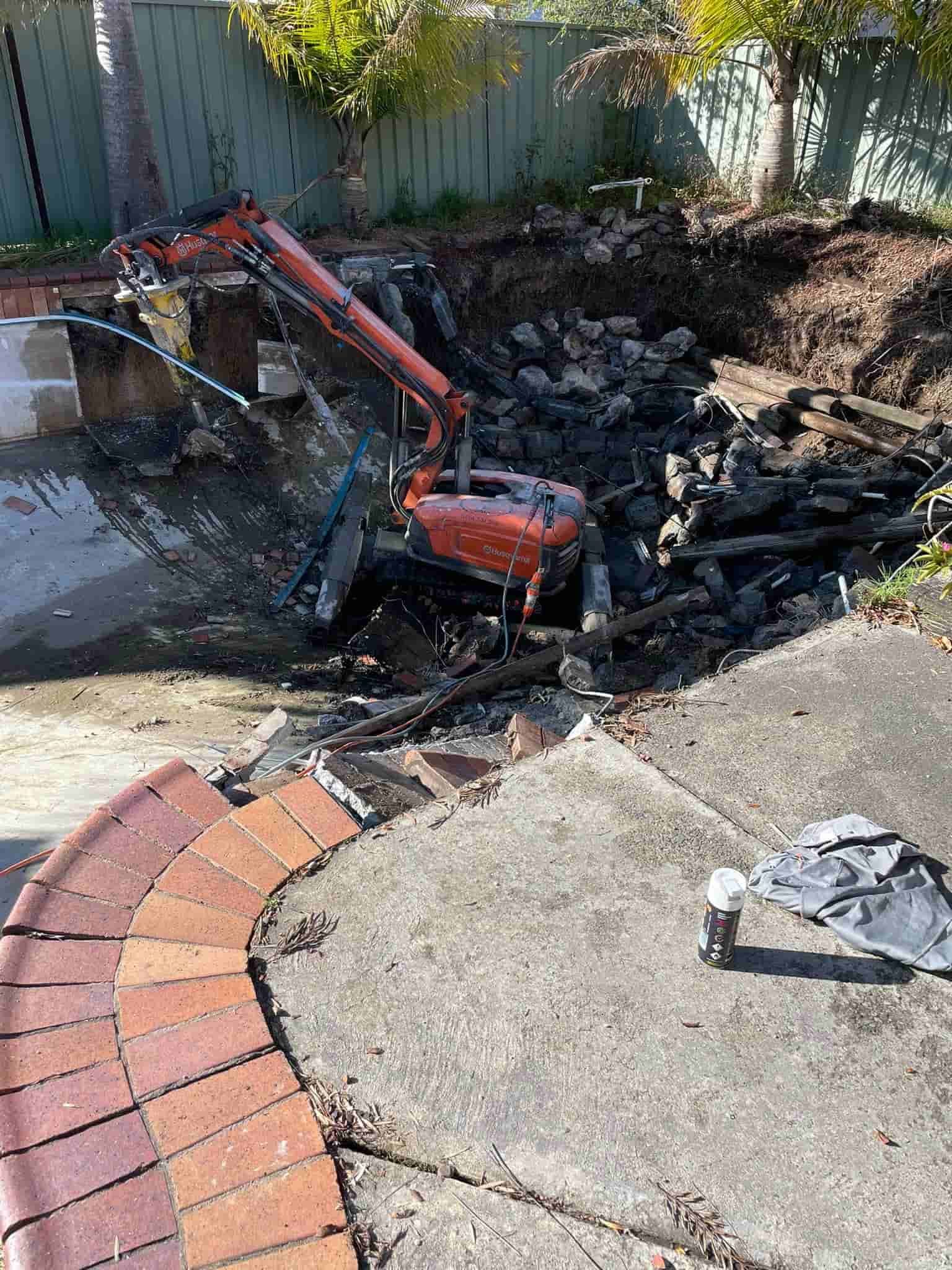 A small excavator is digging a hole in the ground in a backyard — Newcastle Cut & Drill In Boolaroo, NSW