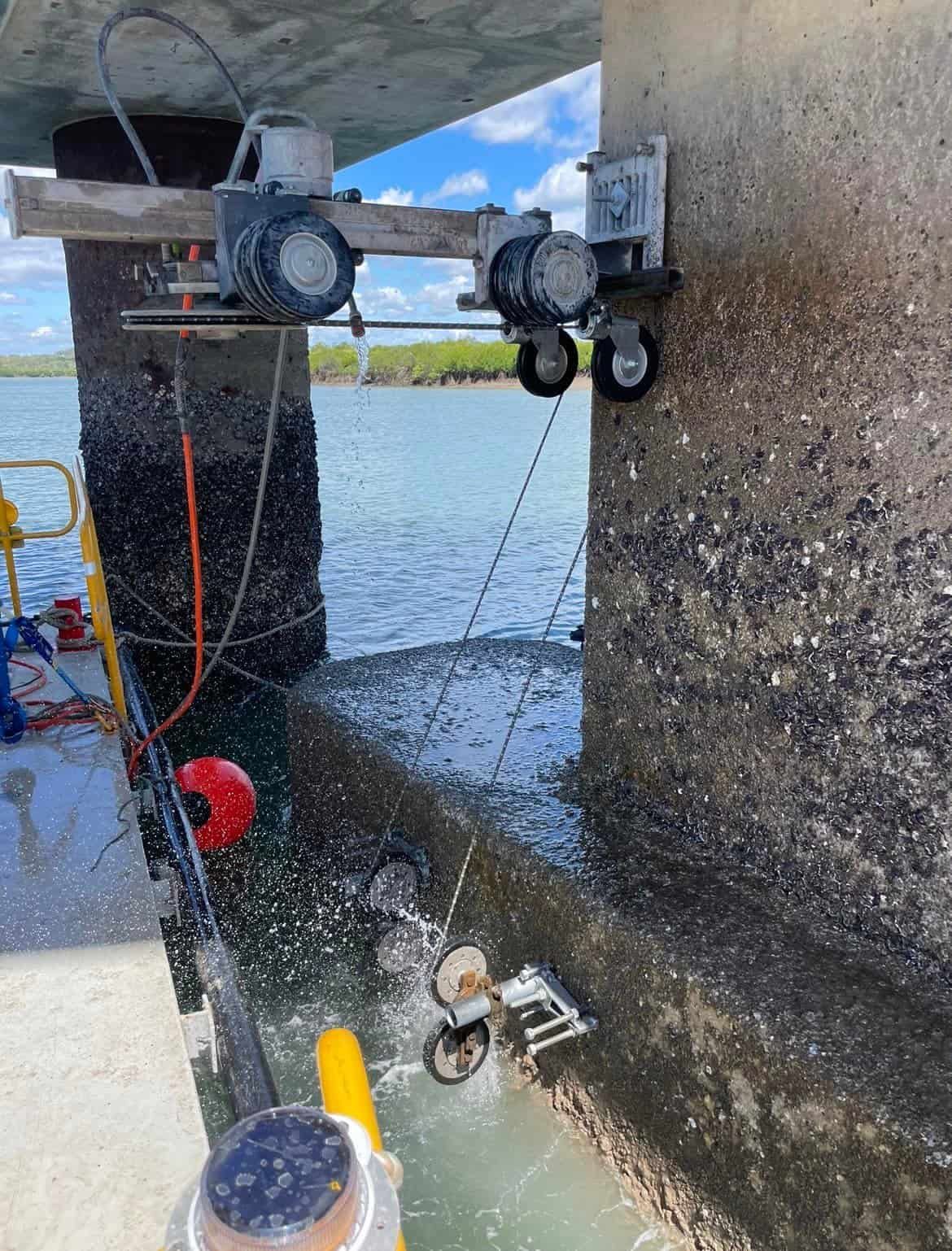 A machine is cutting concrete under a bridge over a body of water — Newcastle Cut & Drill In Boolaroo, NSW