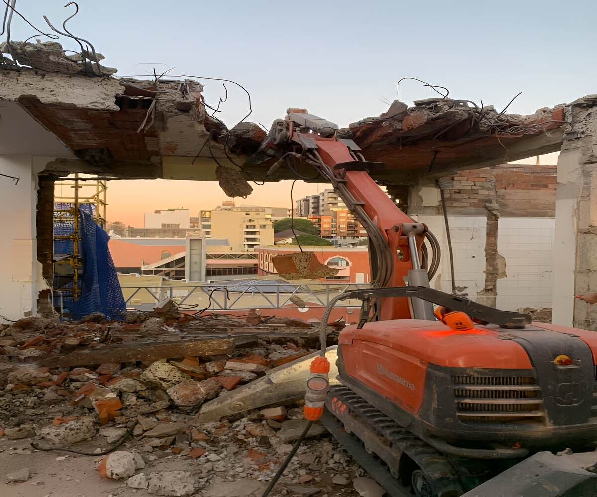 A Bulldozer Is Demolishing A Building With A City In The Background — Newcastle Cut & Drill In Boolaroo, NSW