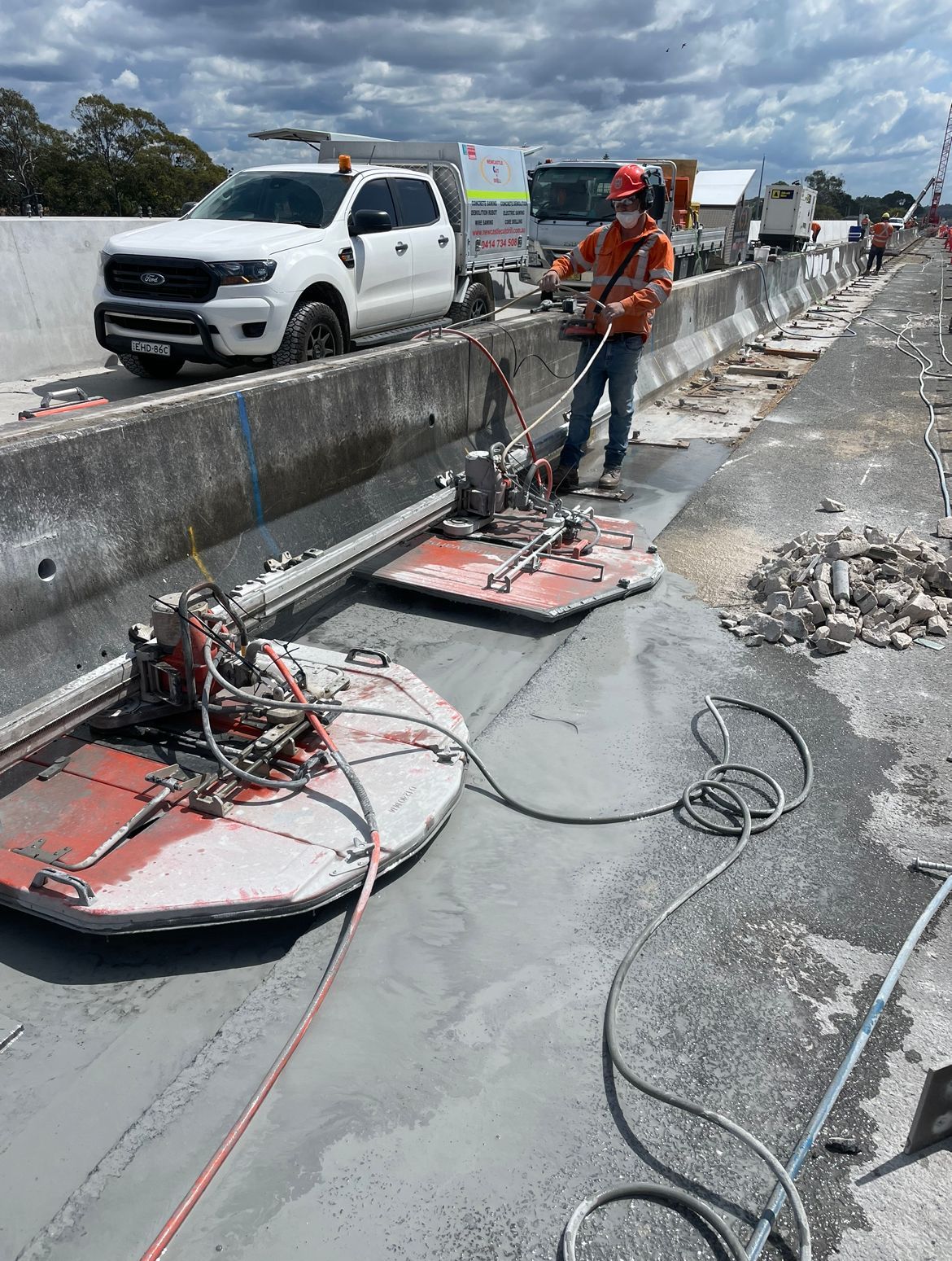 A man is using a Machine Is Cutting A Piece of concrete on the side of a road barrier — Newcastle Cut & Drill In Boolaroo, NSW