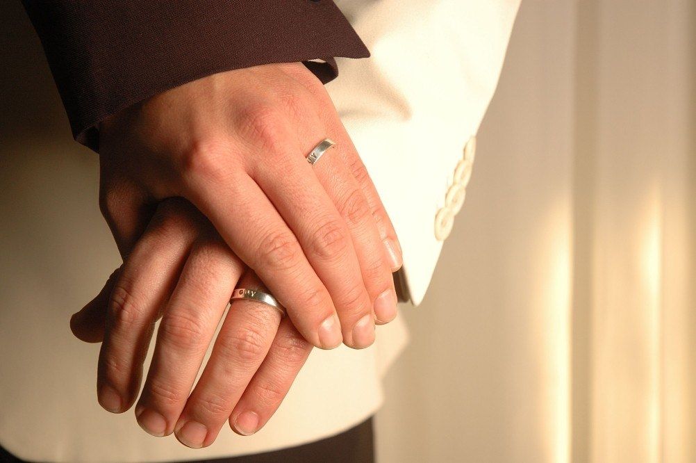 A man wearing a wedding ring holds a woman 's hand