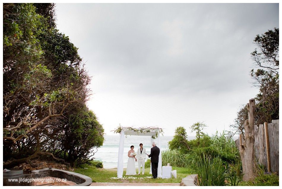 A bride and groom are getting married in front of the ocean.