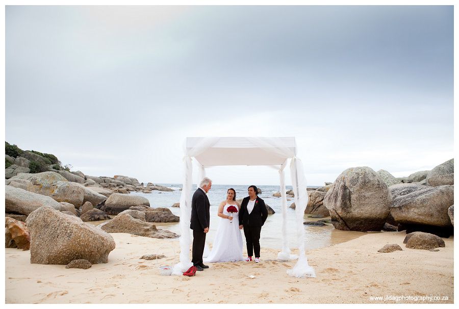 A bride and groom are standing under a white canopy on the beach.