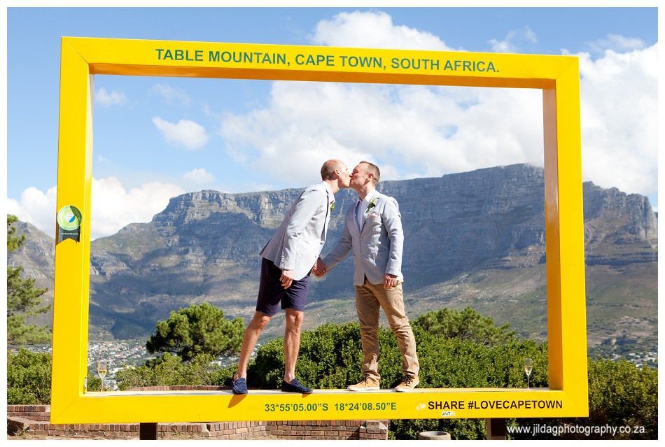 Two men are kissing in front of a mountain in a picture frame.