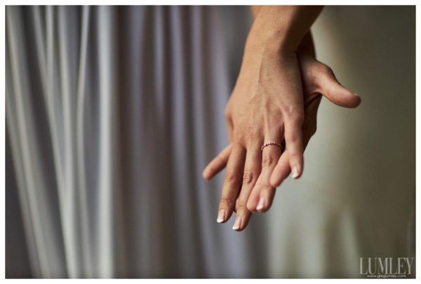 A woman wearing a wedding ring is holding another woman 's hand