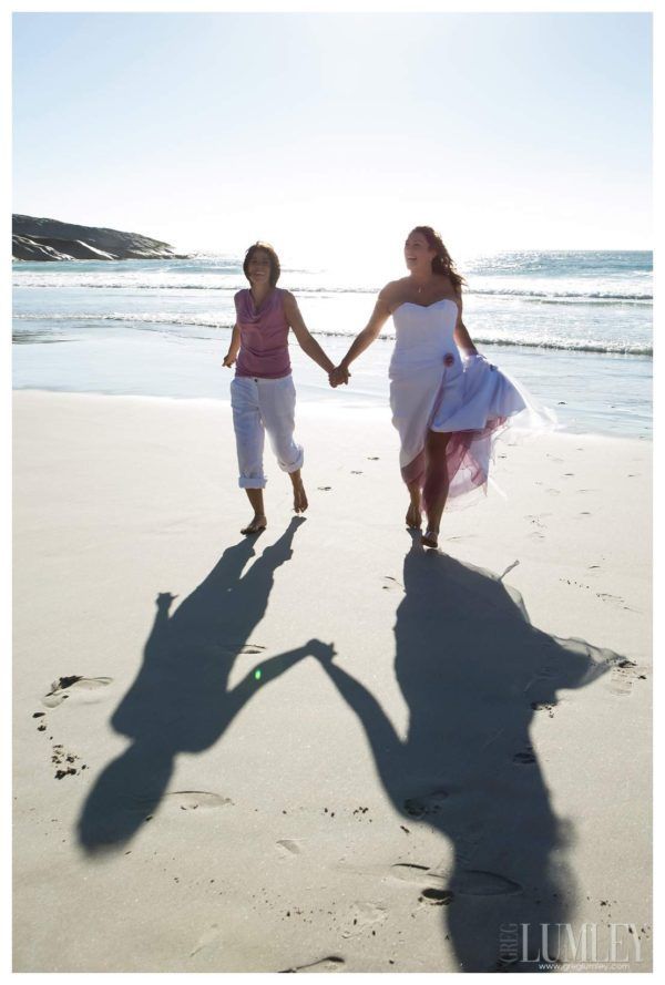 Two women holding hands on the beach with their shadows on the sand