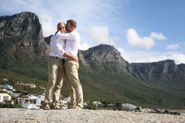 Two men are hugging in front of a mountain.