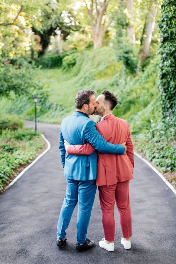 Two men in suits are kissing on the side of a road.