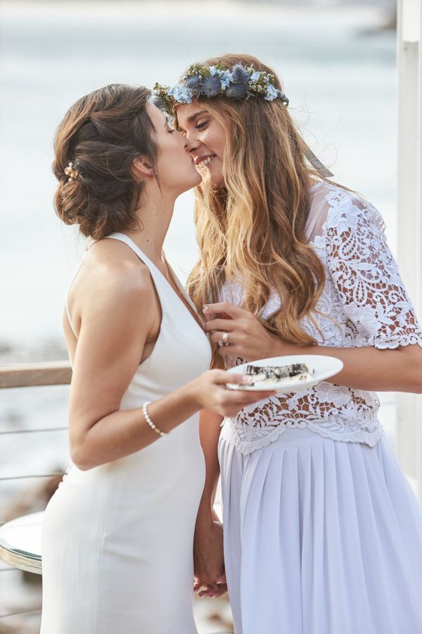 Two women in wedding dresses are kissing each other on the cheek.