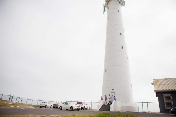 A white lighthouse with cars parked in front of it.