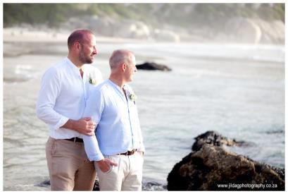 Two men are standing on a beach holding hands.