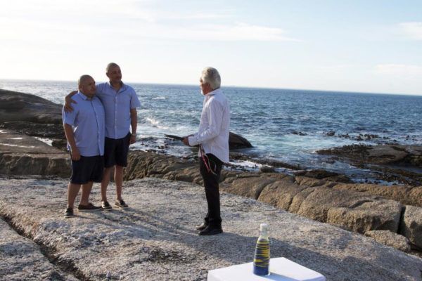 Two men are standing on a rocky beach next to the ocean.