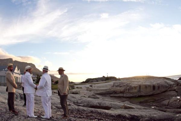 A group of men in white suits and hats are standing on a rocky beach.