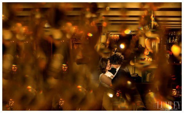 A bride and groom are kissing in a room with a lot of lights.