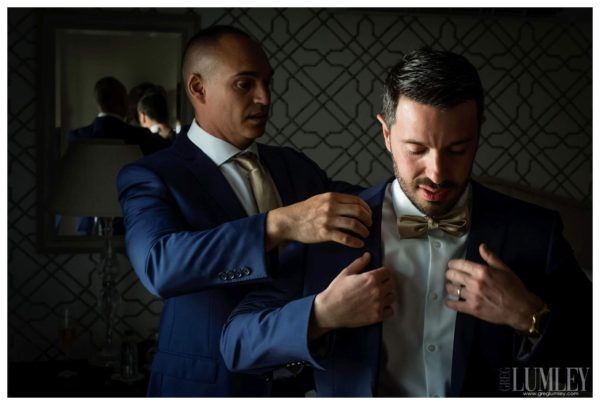 A man in a suit is helping another man with his bow tie.