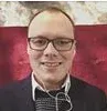 Portrait of a smiling person wearing glasses and a dark shirt against a red background